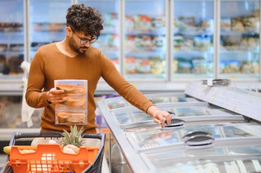 Müşteri markette dondurulmuş ürünler seçiyor, paketlenmiş somon tutuyor ve buzdolabının kapısını açıyor, market alışverişi yapıyor.