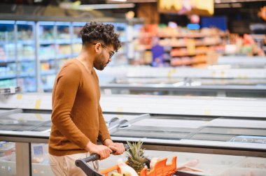 Müşteri, açık bir süpermarket koridorundaki iyi organize edilmiş buzdolabı bölümünden dondurulmuş yiyecek seçerken bir alışveriş arabasını itiyor.