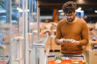 Süpermarket buzdolabı koridorunda alışveriş yaparken gıda etiketi okuyan müşteriler bilgilendirilmiş satın alma kararları alıyorlar.