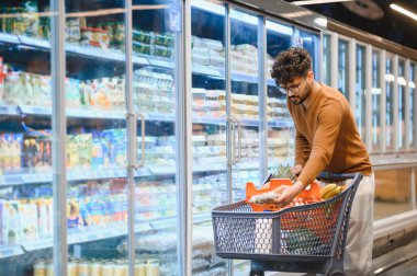 Müşteri dondurulmuş raflardan dondurulmuş ürünleri topluyor, market koridorunda alışveriş arabalarını itiyor.