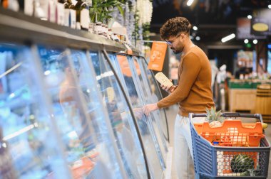 Müşteri dondurulmuş ürünleri süpermarket buzdolabından seçiyor, bir paket tutuyor ve bir alışveriş arabası itiyor.