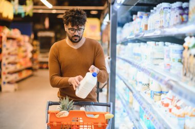 Müşteri marketin buzdolabı bölümünden bir şişe süt seçiyor, market alışverişi yapıyor.