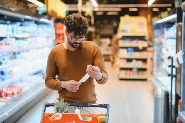 Süpermarket koridorunda alışveriş fişini kontrol eden, harcamaları yöneten ve doğru fatura kesen odaklı müşteri