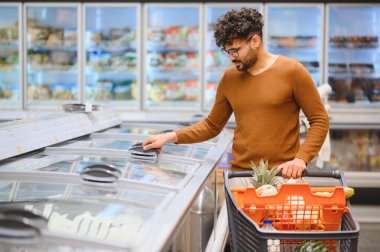 Müşteri dondurulmuş ürünleri marketteki dondurulmuş bir koridordan seçiyor, sağlıklı beslenmek için çeşitli seçenekleri gözden geçiriyor.