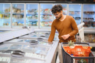 Müşteri dondurulmuş ürünleri süpermarket buzdolabından seçiyor, bakkaliye ve yemek malzemeleri alırken koridorlarda geziniyor.