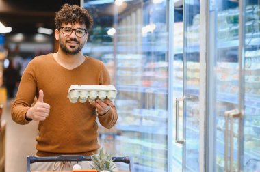 Müşteri süpermarkette bir kutu yumurtayı tutarken elini kaldırıyor, taze yiyecek almaktan memnun oluyor.