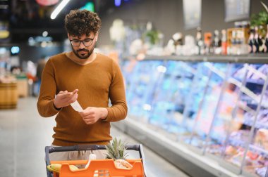 Parlak bir süpermarkette artan market maliyetleri arasında alışveriş makbuzunu gözden geçirir, bütçeyi yönetir.