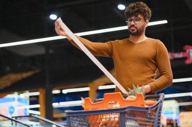 Müşteri, markette alışveriş arabasıyla alışveriş yaparken çok uzun bir faturasını kontrol ediyor.