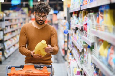 Müşteri, bakkal koridorunda yürürken sarı bir şişeyle ürün bilgilerini okuyor sağlıklı bir yaşam tarzı için düşünceli seçimler yapıyor.