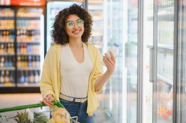 Müşteri gülümseyerek marketin soğutuculu bölümünden bir şişe süt seçiyor ve sağlıklı bir alışveriş deneyimi yaşıyor.