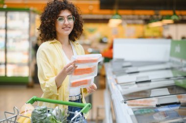 Müşteri marketten alışveriş yapıyor, donmuş somon paketleri tutuyor, alışveriş arabası satıyor.