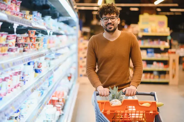 Genç Arap adam marketin koridorlarında dolanıp alışveriş deneyiminin tadını çıkarırken market arabalarını itiyor.
