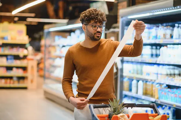 Markette alışveriş yaparken çok uzun bir makbuzu inceleyen müşteri, ürünlerin yüksek maliyetine şaşırır.
