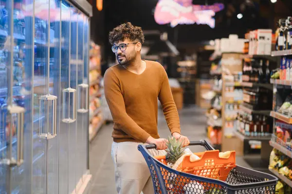 Müşteri alışveriş arabasını iterken markette taze yiyecekler seçiyor. Ürünlerle dolu koridorlarda geziniyor.