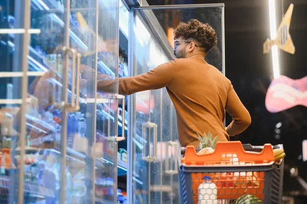 Arap adam süpermarkette alışveriş yapıyor, buzdolabının kapısını açıyor ve dondurulmuş gıdayı seçiyor.