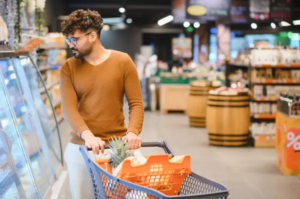 Genç bir Arap alışveriş arabasını iterken marketin yoğun bir koridorunda dondurulmuş yiyecek seçiyor.