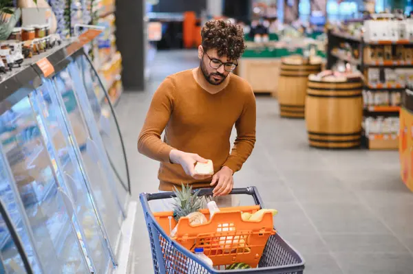 Genç Arap adam market alışverişi yapıyor. Süpermarketten dondurulmuş yiyecekleri seçiyor.