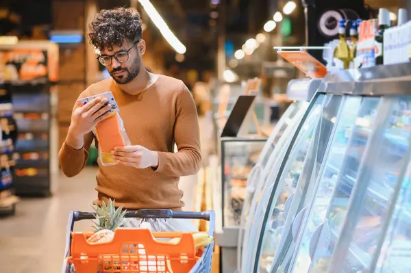 Markette yiyecek seçen genç bir adam, sağlıklı yiyecek için alışveriş yaparken somon paketinin etiketini inceliyor.