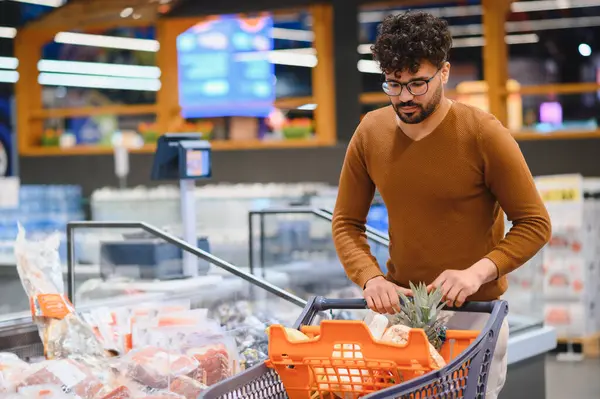 Müşteri yiyecek alıyor, markette alışveriş arabası satıyor, dondurulmuş ürünleri kontrol ediyor.