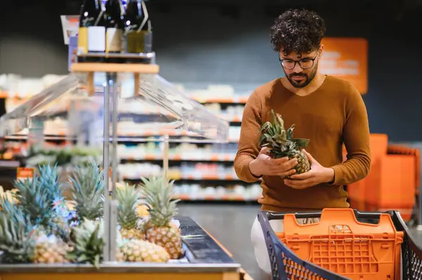 Müşteri süpermarketten taze ananas seçiyor, alışveriş sepeti tutuyor ve market alışverişi yapıyor.