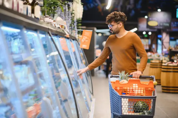 Müşteri dondurulmuş yiyecekleri süpermarketteki soğutuculu vitrinden seçiyor, alışveriş arabasını markete doğru itiyor.