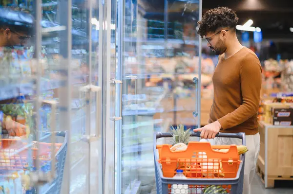 Müşteri dondurulmuş yiyecek alıyor, süpermarkette alışveriş arabası satıyor, buzdolabında yiyecek seçiyor.