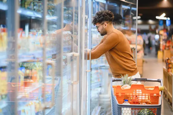 Müşteri buzdolabının kapısını açıyor, markette dondurulmuş ürünleri seçiyor, alışveriş yapıyor.