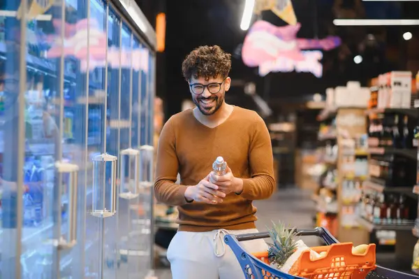 Marketten yiyecek seçen, elinde bir şişe su tutan ve gülümseyen mutlu bir müşteri.