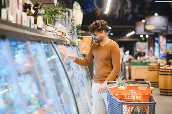 Müşteri markette dondurulmuş yiyecekleri seçiyor, alışveriş arabasını taze ürünlerle dolduruyor.