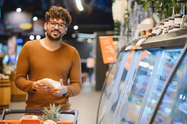 Müşteri, marketin fırın bölümünden ekmek seçiyor, alışveriş arabasını taze ürünlerle itiyor.