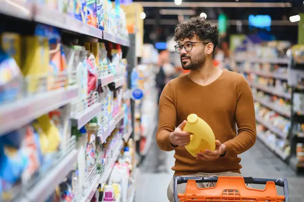 Müşteri süpermarkette deterjan şişesini seçiyor, marketten alışveriş yaparken etiketi dikkatlice okuyor.