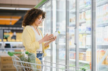 Müşteri bakkaldaki bir süt şişesinin içeriğini ve besin bilgilerini okuyarak sağlıklı yiyecekler hakkında bilgilendirici seçimler yapıyor.