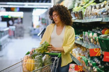 Müşteri süpermarkette alışveriş yaparken taze marul seçiyor, sağlıklı yiyeceklerle dolu.