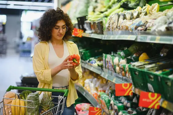 Müşteri marketten taze ürünler seçiyor, alışveriş yaparken kırmızı dolma biber tutuyor.