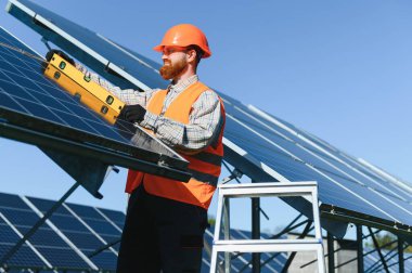 Güneş enerjisi geçişi üzerinde çalışan, bir güneş enerjisi istasyonuna güneş panelleri kurarken seviye aracı kullanan mühendis