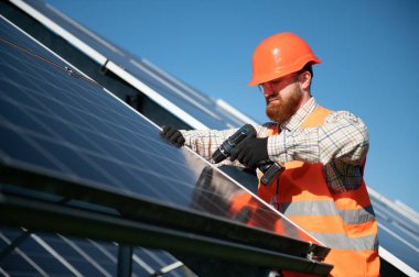 Fotovoltaik bir fabrikada çalışan yetenekli bir teknisyen tornavida kullanarak güneş panelleri kuruyor ve yenilenebilir enerji üretimine katkıda bulunuyor.