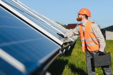 Güneş enerjisi santralinde çalışan mühendis alet çantası taşıyor ve yenilenebilir enerji için fotovoltaik paneller kuruyor.