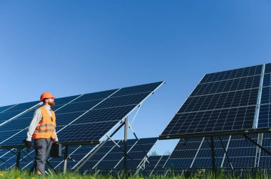 Güneş paneli çiftliğini inceleyen elektrik mühendisi mavi gökyüzü güneşli bir günde bir alet çantası taşıyor.