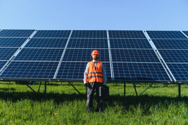Güvenlik donanımlı erkek işçi güneş panellerinin önünde duruyor, yenilenebilir enerji sektöründeki kurulum ve onarımları vurguluyor