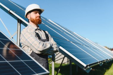 Çapraz kollu erkek mühendis ve güneş panellerinin yenilenebilir enerji üretimi için bir fotovoltaik fabrikaya kurulmasını denetleyen sert şapka