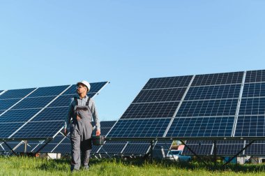 Bir fotovoltaik elektrik santralinin bakımını üstlenen ve bakımını yapan bir alet çantası taşıyan, güneş panelleri arasında yürüyen orta doğu mühendisi.