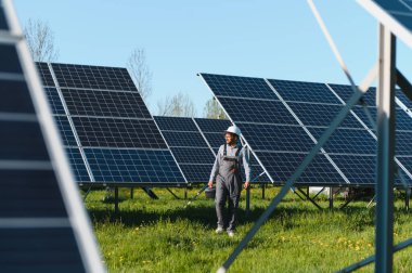 Ortadoğu mühendisi güneş paneli çiftliğinde yürüyor, aletler taşıyor ve tulum ve güvenlik kaskı takıyor.