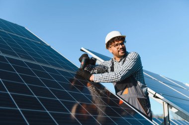 Mavi gökyüzü güneşli bir günde tornavida kullanarak bir enerji santralinde ekolojik güneş paneli kurulumu üzerinde çalışan Ortadoğu mühendisi.