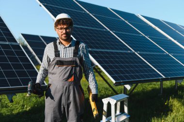 Mühendis, güneş panellerinin kurulumu ve bakımı üzerine çalışan bir güneş çiftliğinde bir matkap ve seviye tutuyor.