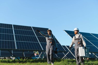 Bir güneş enerjisi santralinde yürüyen ve çalışan iki mühendis, fotovoltaik paneller kuruyor veya onarıyor