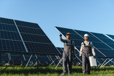 Bir güneş enerjisi santralinde çalışan iki mühendis yenilenebilir enerji üretimi için güneş panelleri kuruyor ve koruyorlar.
