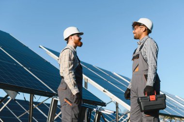 Güneşli bir günde güneş panellerini büyük bir alana yerleştirirken sonraki adımları tartışan iki mühendis.