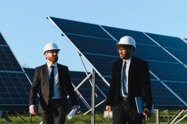 Güneş çiftliğinde güneş panellerinin yanında yürüyen ve tartışan takım elbiseli iki işadamı.
