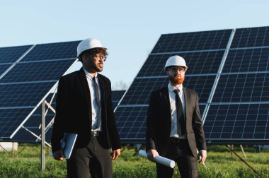 Bir güneş paneli çiftliğinde yürüyen ve denetleyen iki mühendis yenilenebilir enerji ve sürdürülebilirlik çözümlerini tartışıyor.
