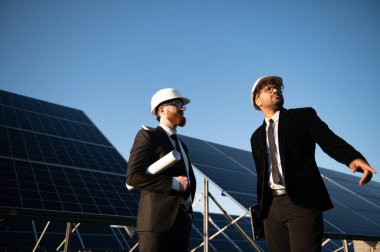 İki mühendis güneş enerjisi çiftliğinde sürdürülebilir enerji çözümleri üzerinde çalışan bir projeyi tartışıyor.